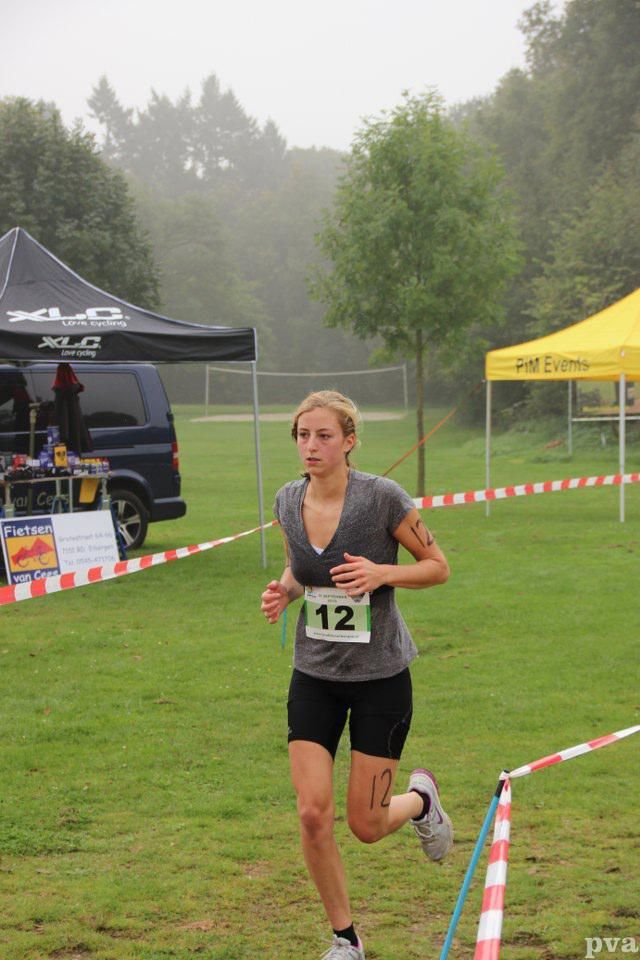 Triathlon Eibergen. Een vrouw rent door een veld met het nummer 12 op haar shirt.
