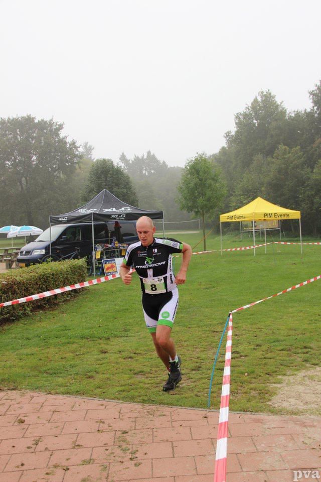 Triathlon Eibergen. Een man rent door een veld met op de achtergrond een gele tent.