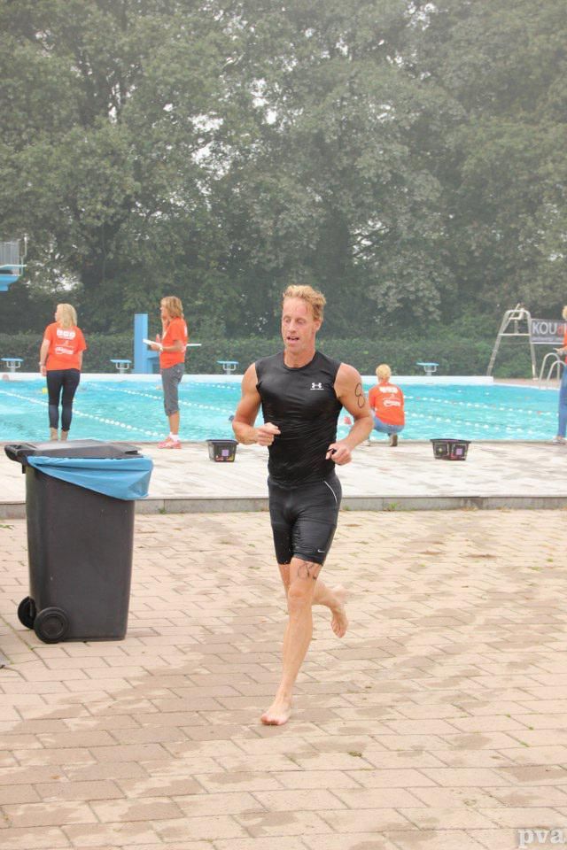 Triathlon Eibergen. Een man rent op blote voeten voor een zwembad.