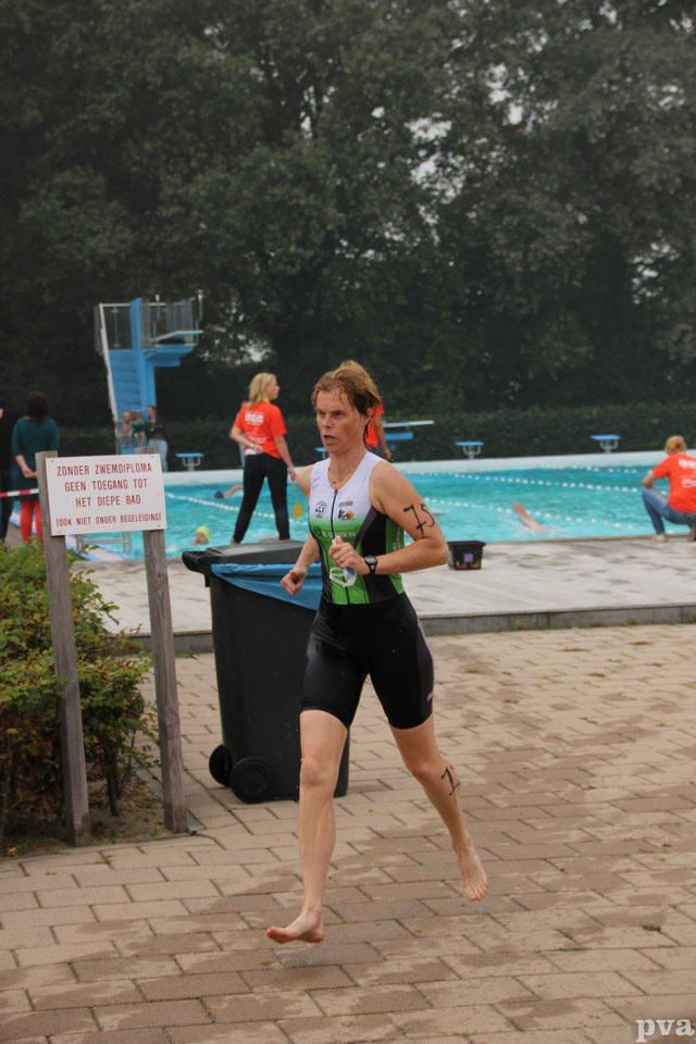 Triathlon Eibergen. Een vrouw rent op blote voeten voor een zwembad.