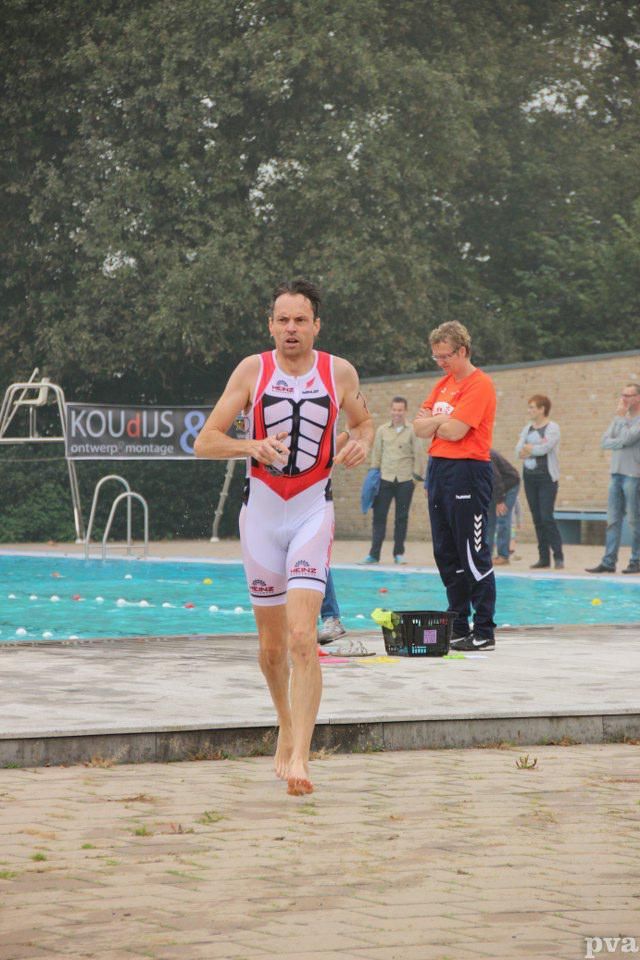 Triathlon Eibergen. Een man rent op blote voeten voor een zwembad.