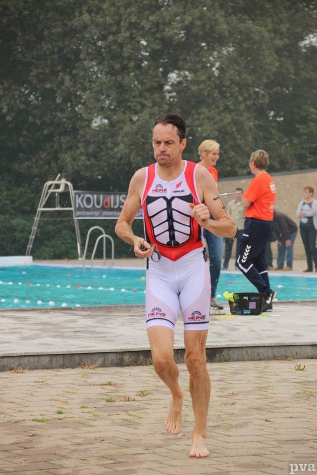 Triathlon Eibergen. Een man rent op blote voeten voor een zwembad.