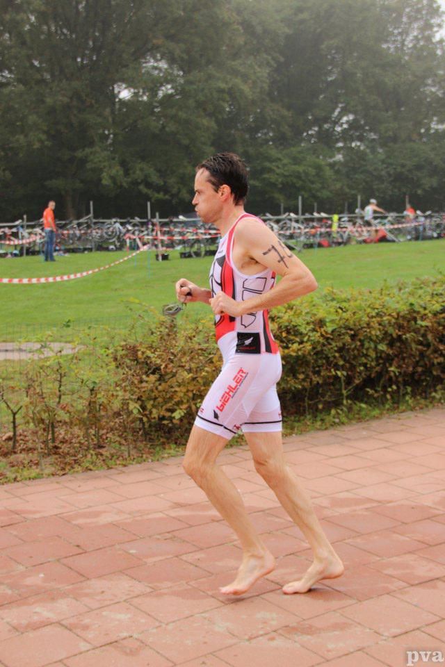 Triathlon Eibergen. Een man in een triatlonpak rent op blote voeten