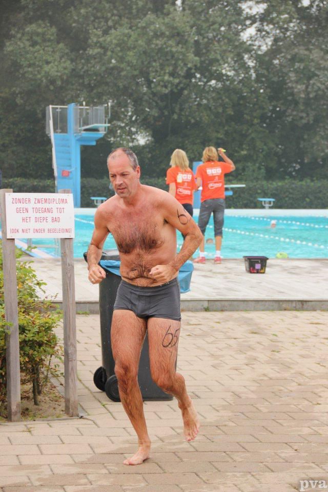 Triathlon Eibergen. Een man zonder shirt rent voor een zwembad.