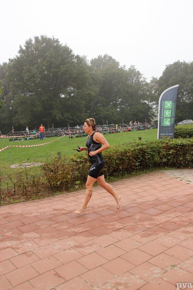 Triathlon Eibergen. Een vrouw rent op blote voeten op de stoep in een park.