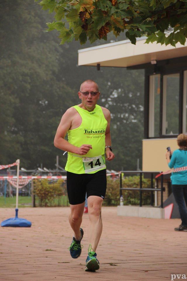 Een man in een geel tanktopje en een zwarte korte broek doet mee aan een race.