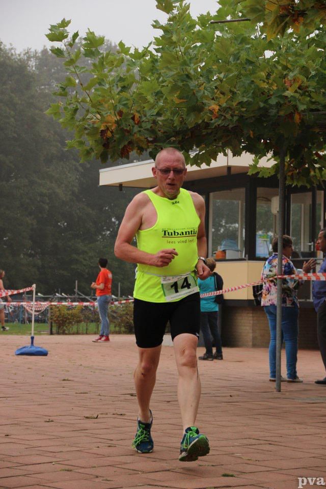 Een man in een neongeel tanktopje en een zwarte korte broek rent een race.