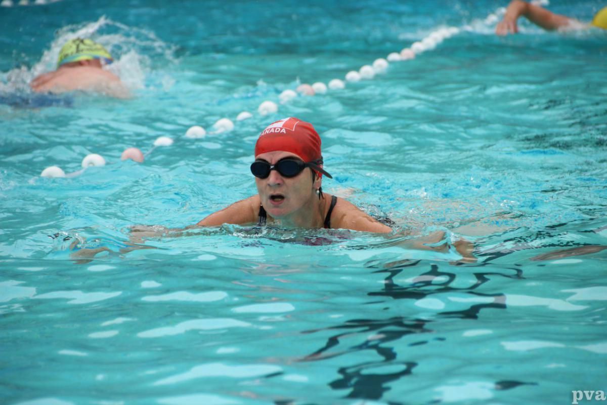 Een vrouw zwemt in een zwembad met een rode pet en een zonnebril op.