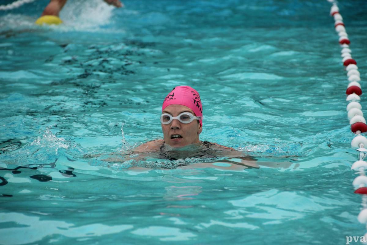 Een vrouw met een roze badmuts en een zwembril zwemt in een zwembad.