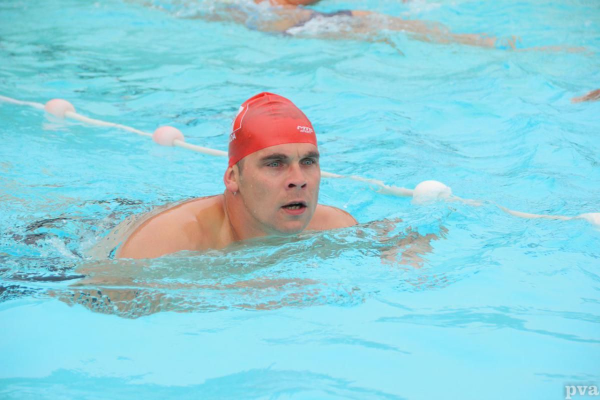 Een man met een rode badmuts zwemt in een zwembad.