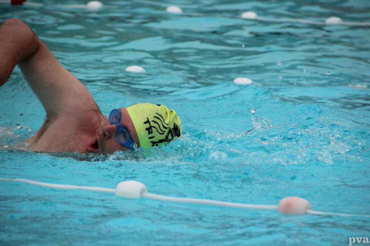 Een man met een gele badmuts zwemt in een zwembad.
