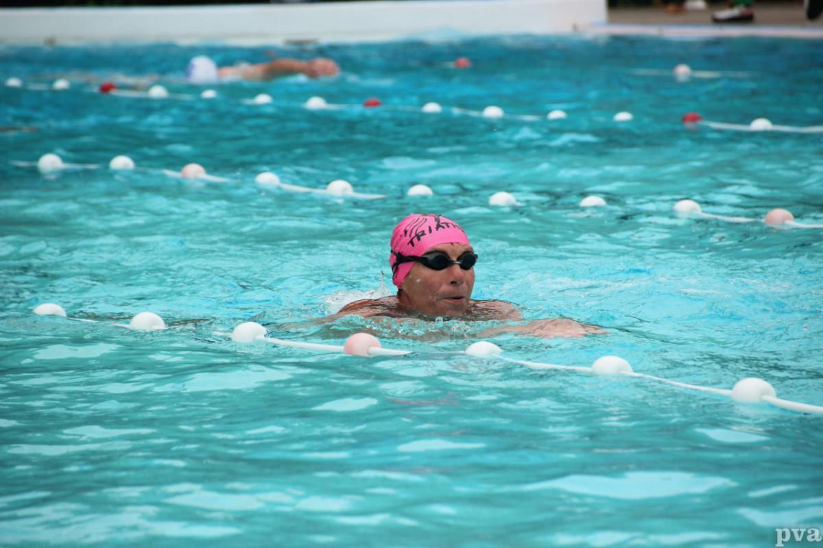 Een man zwemt in een zwembad met een roze badmuts en een zwembril.