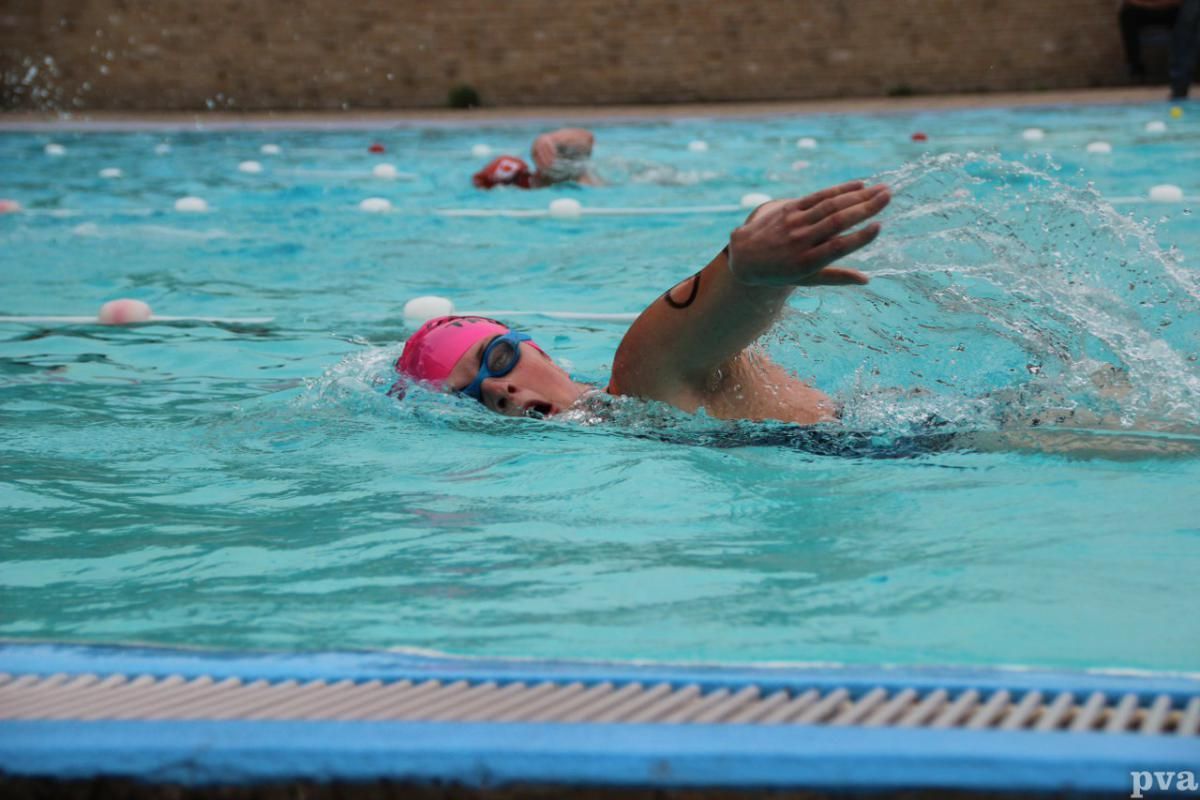 Een vrouw zwemt in een zwembad met een roze badmuts en een zwembril.
