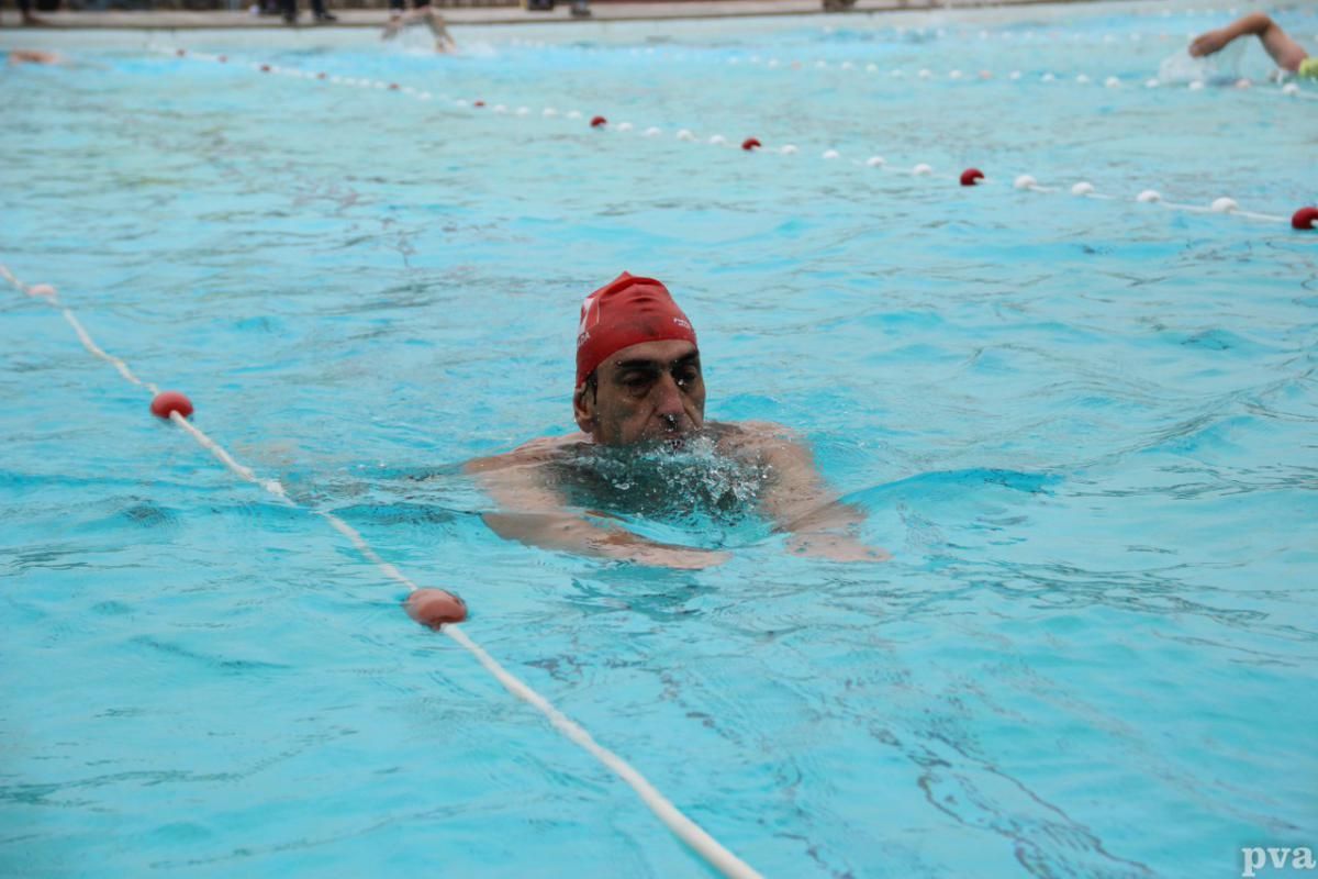 Een man met een rode badmuts zwemt in een zwembad.