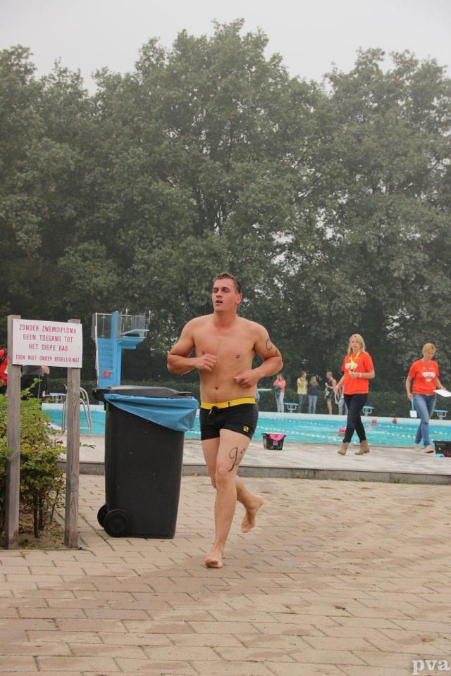Een man zonder shirt rent op blote voeten voor een zwembad.