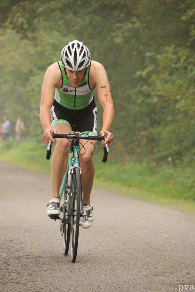 Een man met een helm rijdt op een fiets over de weg.