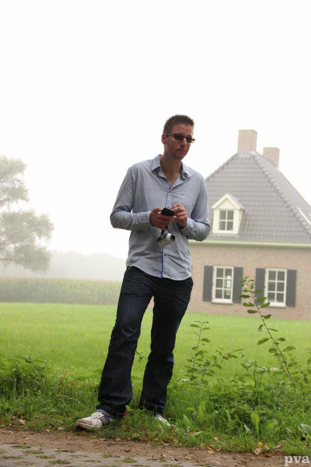 Een man staat voor een huis en houdt een camera vast.