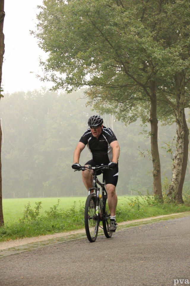 Triathlon Eibergen. Een man fietst over een weg met bomen op de achtergrond
