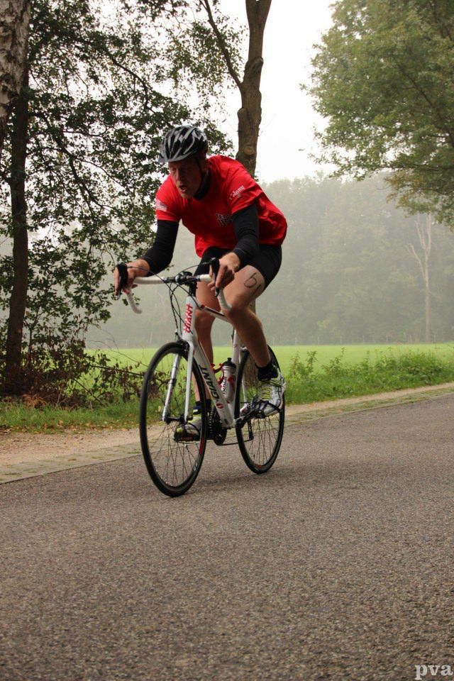 Triathlon Eibergen. Een man in een rood shirt fietst over een weg.