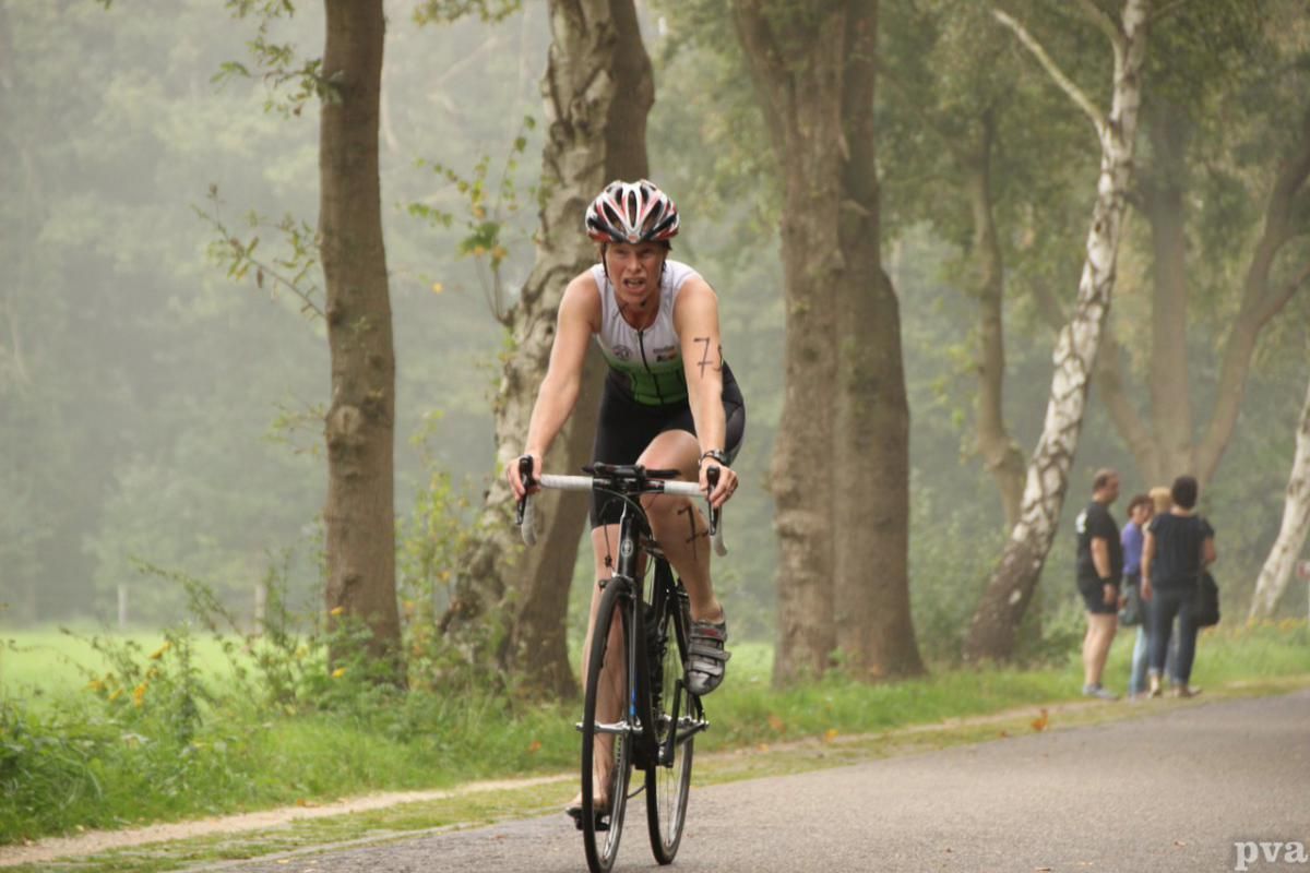Triathlon Eibergen. Een vrouw fietst over een weg in het bos.