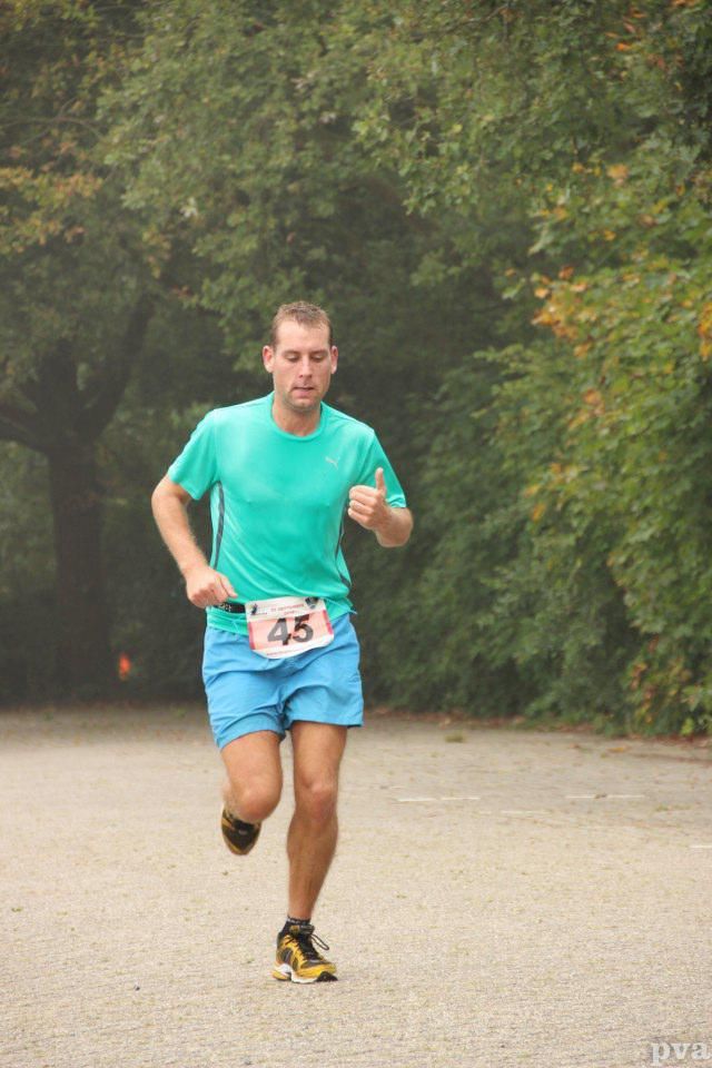 Triathlon Eibergen. Een man in een groen shirt en een blauwe korte broek rent in een park.