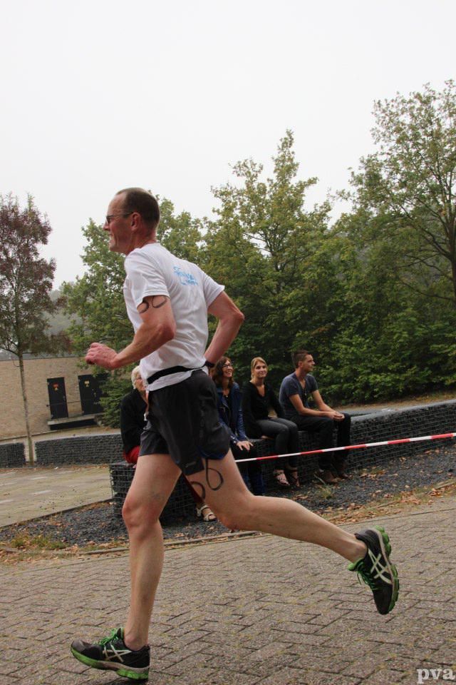 Triathlon Eibergen. Een man in een wit overhemd en een zwarte korte broek rent over een stenen weg.