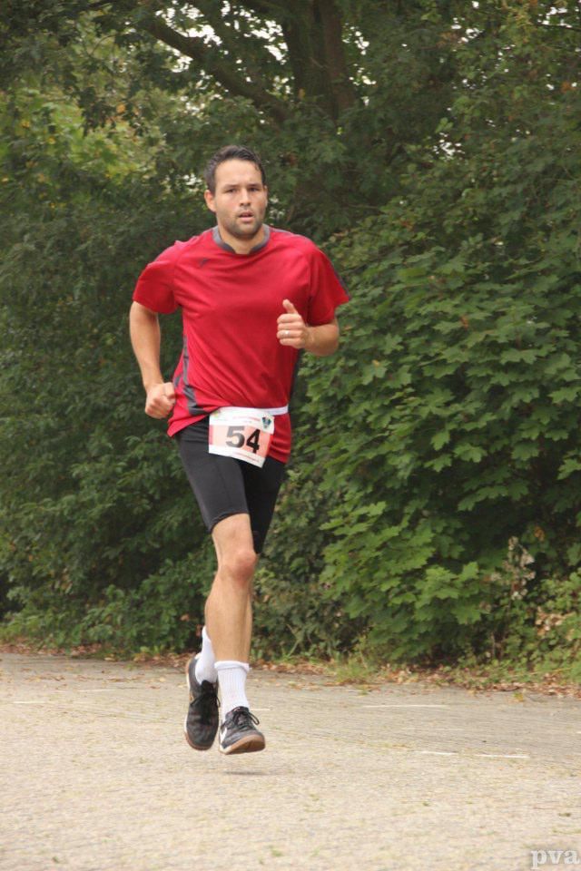 Triathlon Eibergen. Een man in een rood shirt en een zwarte korte broek rent over de weg.