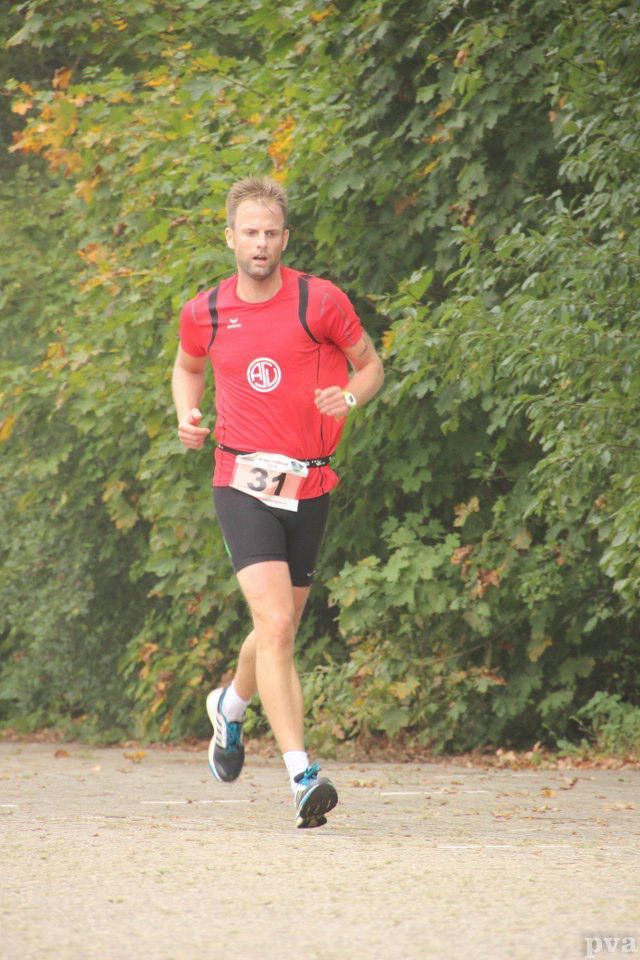 Triathlon Eibergen. Een man in een rood shirt en een zwarte korte broek rent over de weg.