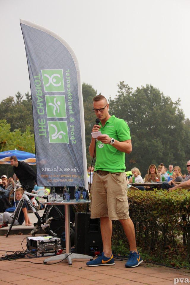 Een man in een groen shirt staat voor een publiek met een microfoon in zijn handen.