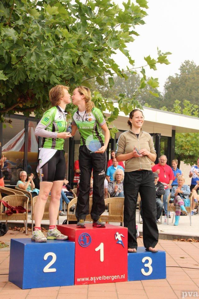 Twee vrouwen kussen elkaar op een podium met daarop het getal 2 en 3