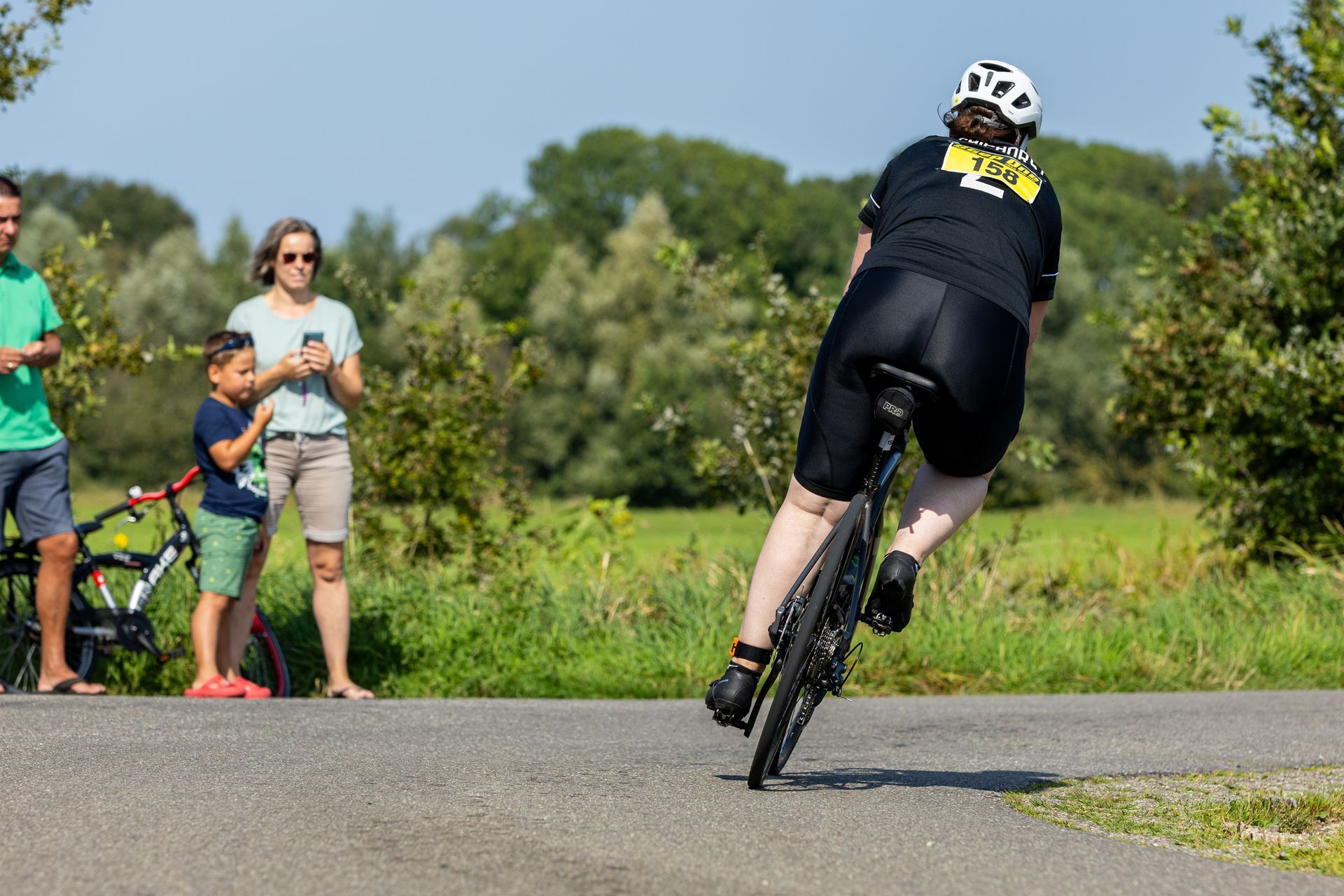 Een vrouw fietst over een weg terwijl een groep mensen toekijkt.