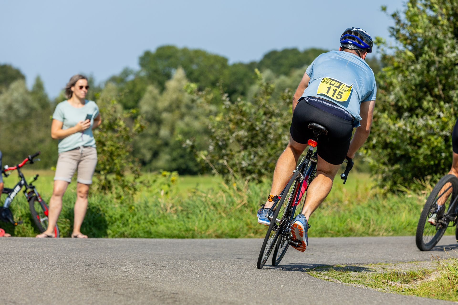 Een man fietst over een weg terwijl een vrouw toekijkt.