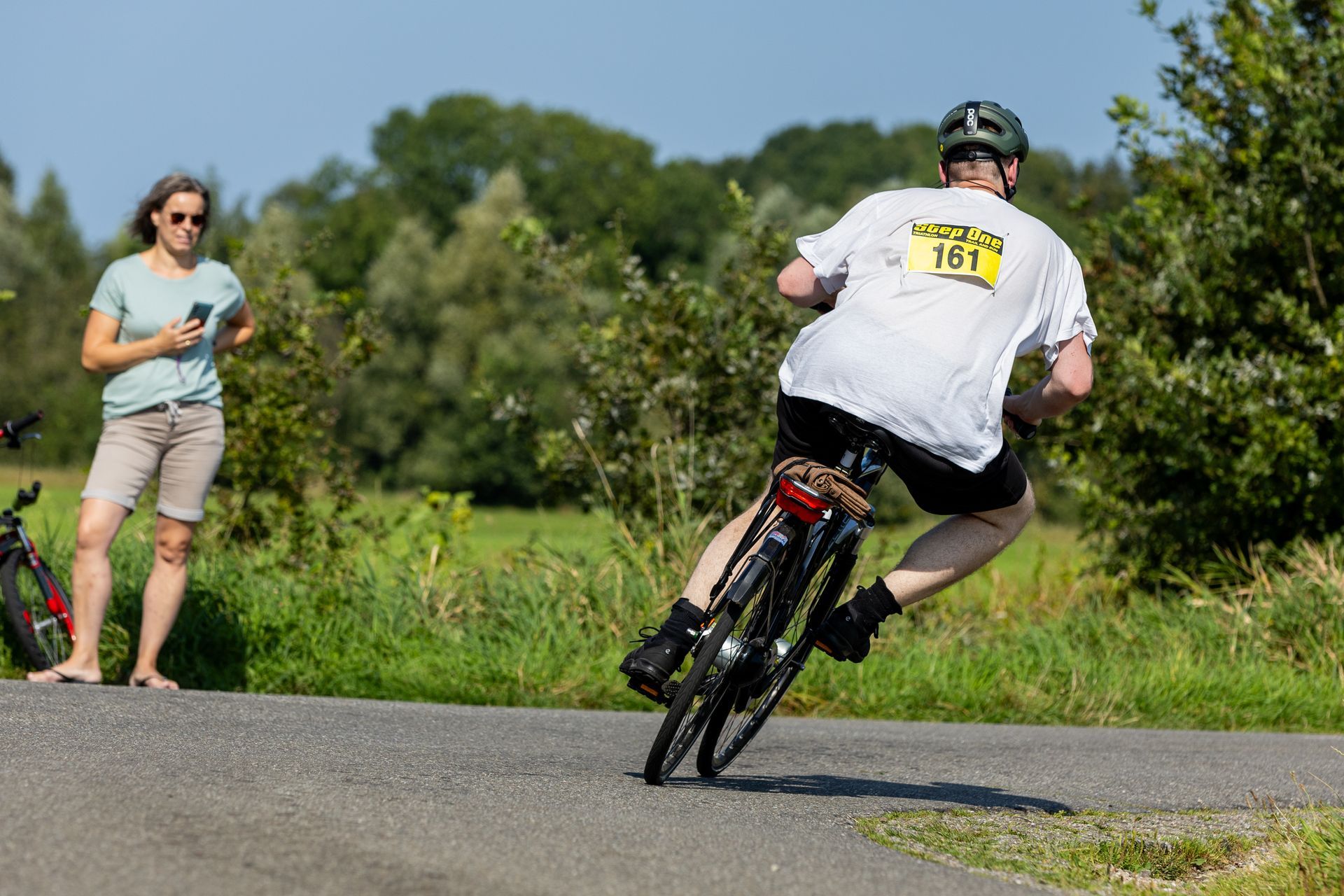 Een man fietst over een weg terwijl een vrouw toekijkt.