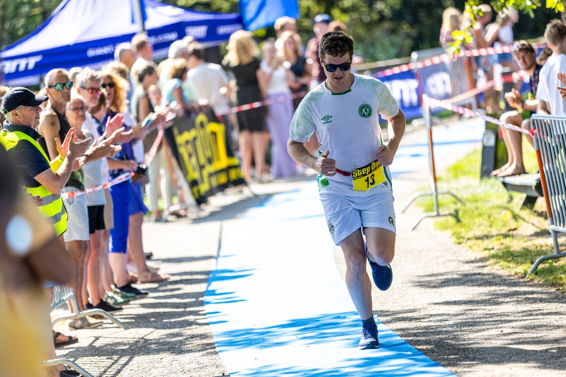 Een man rent over een blauwe loper voor een menigte mensen.