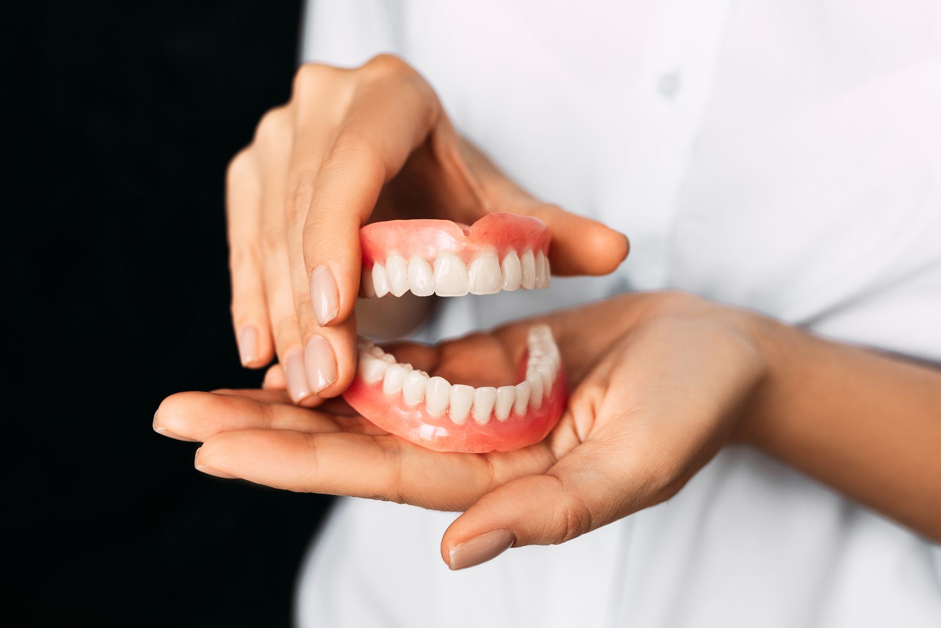 Close-up of a dentist holding a complete denture model in his hands.