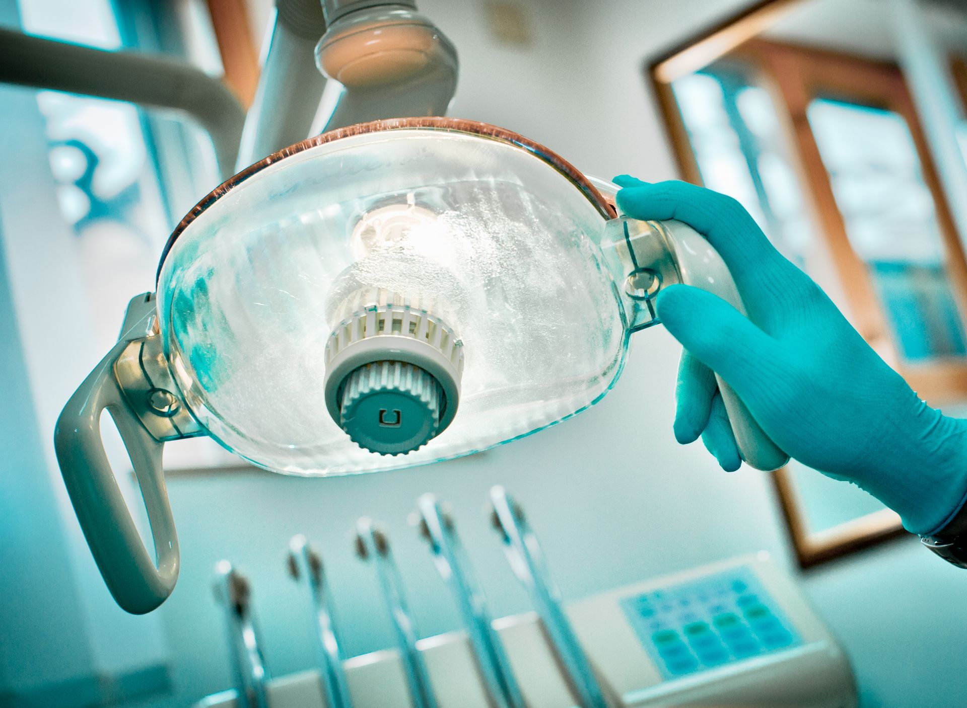 Dentist adjusting lamp in office, wearing blue glove.