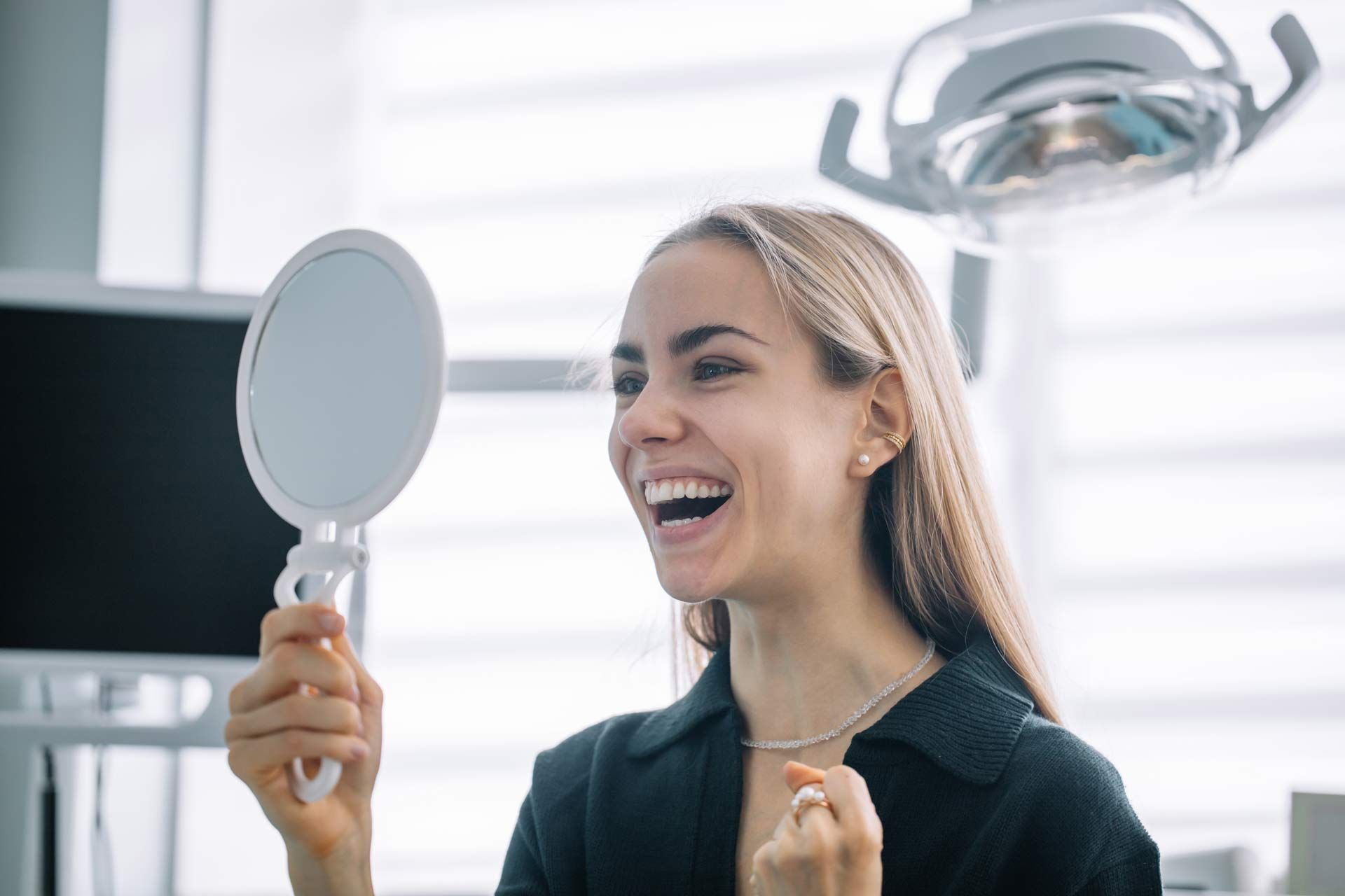 Person examines their smile with a mirror in a dental office