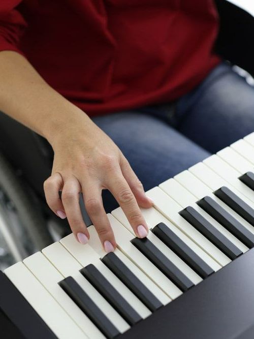 A Woman In A Wheelchair Is Playing A Piano — Doug Simpson Piano Tuning In Gordonvale, QLD