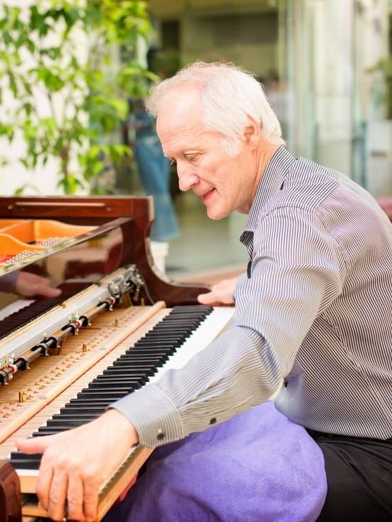 A Man In A Striped Shirt Is Playing A Piano — Doug Simpson Piano Tuning In Manunda, QLD