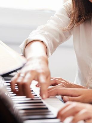 A Woman In A White Shirt Is Playing A Piano — Doug Simpson Piano Tuning In Manunda, QLD