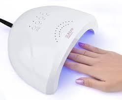 Secador de uñas blanco con una mano en su interior, secando esmalte de uñas en gel morado.