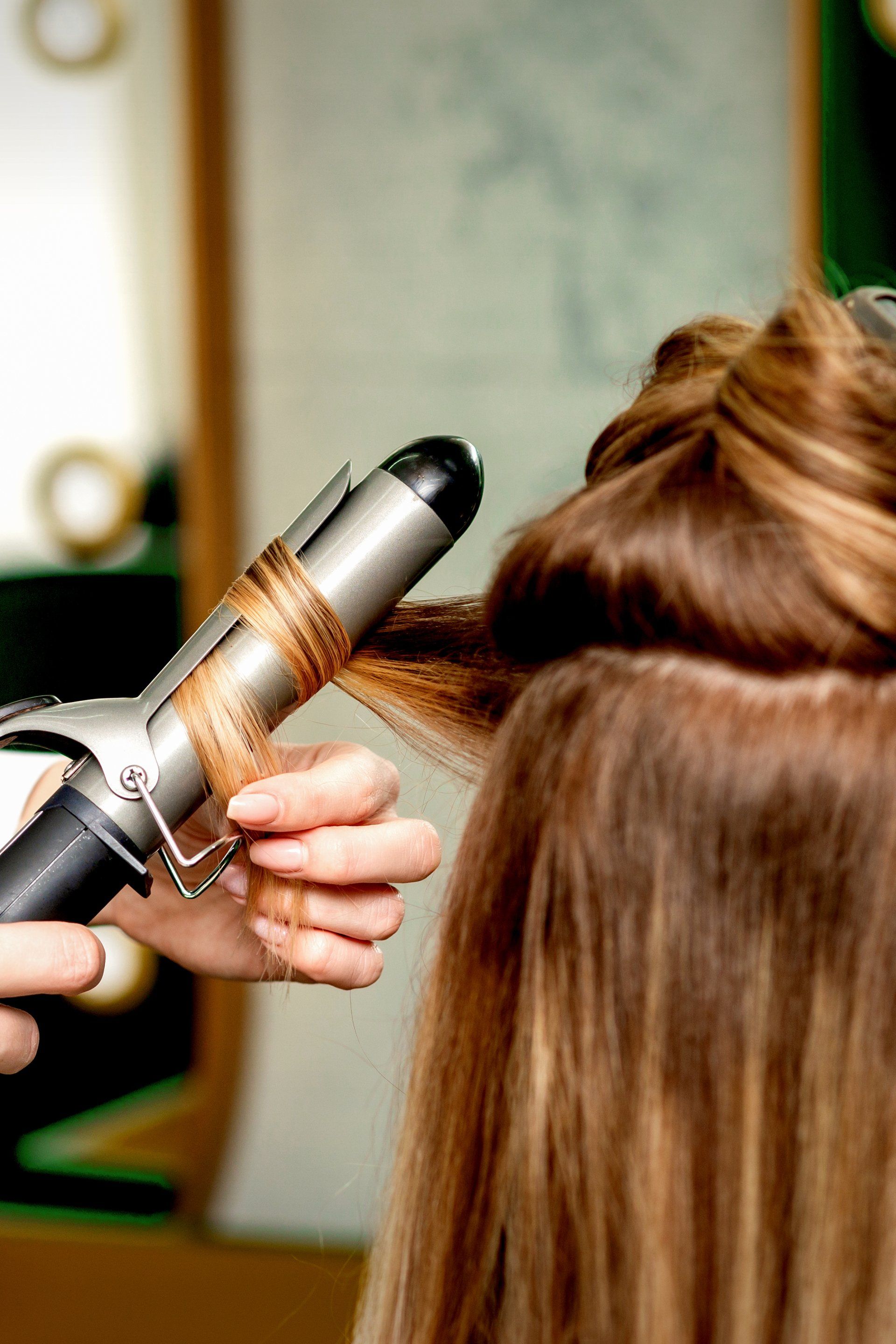 Curling iron styling brown hair in a salon.