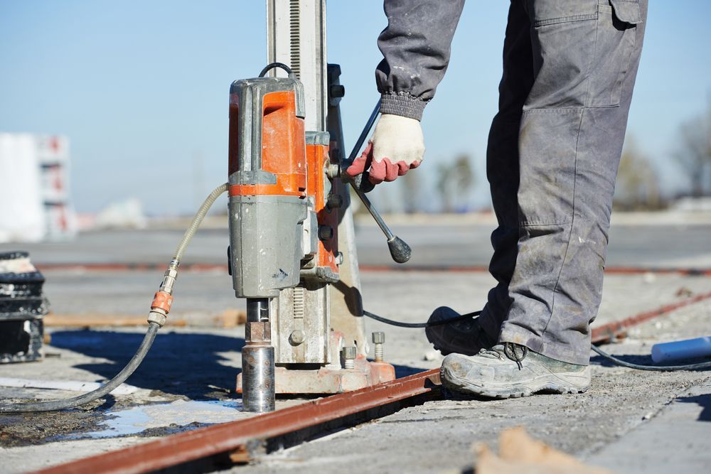 A Man Is Using A Drill On A Construction Site — The Rectifiers In Robina, QLD