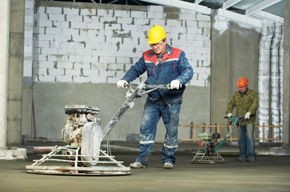 A Construction Worker Is Using A Machine To Smooth The Concrete Floor — The Rectifiers In Robina, QLD
