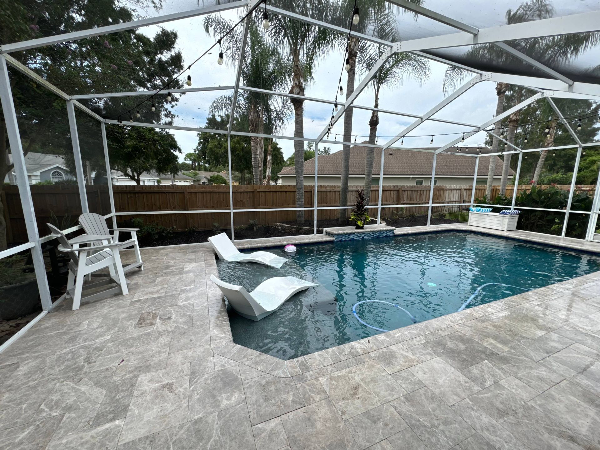 Pool area with screened enclosure, chairs, and string lights.