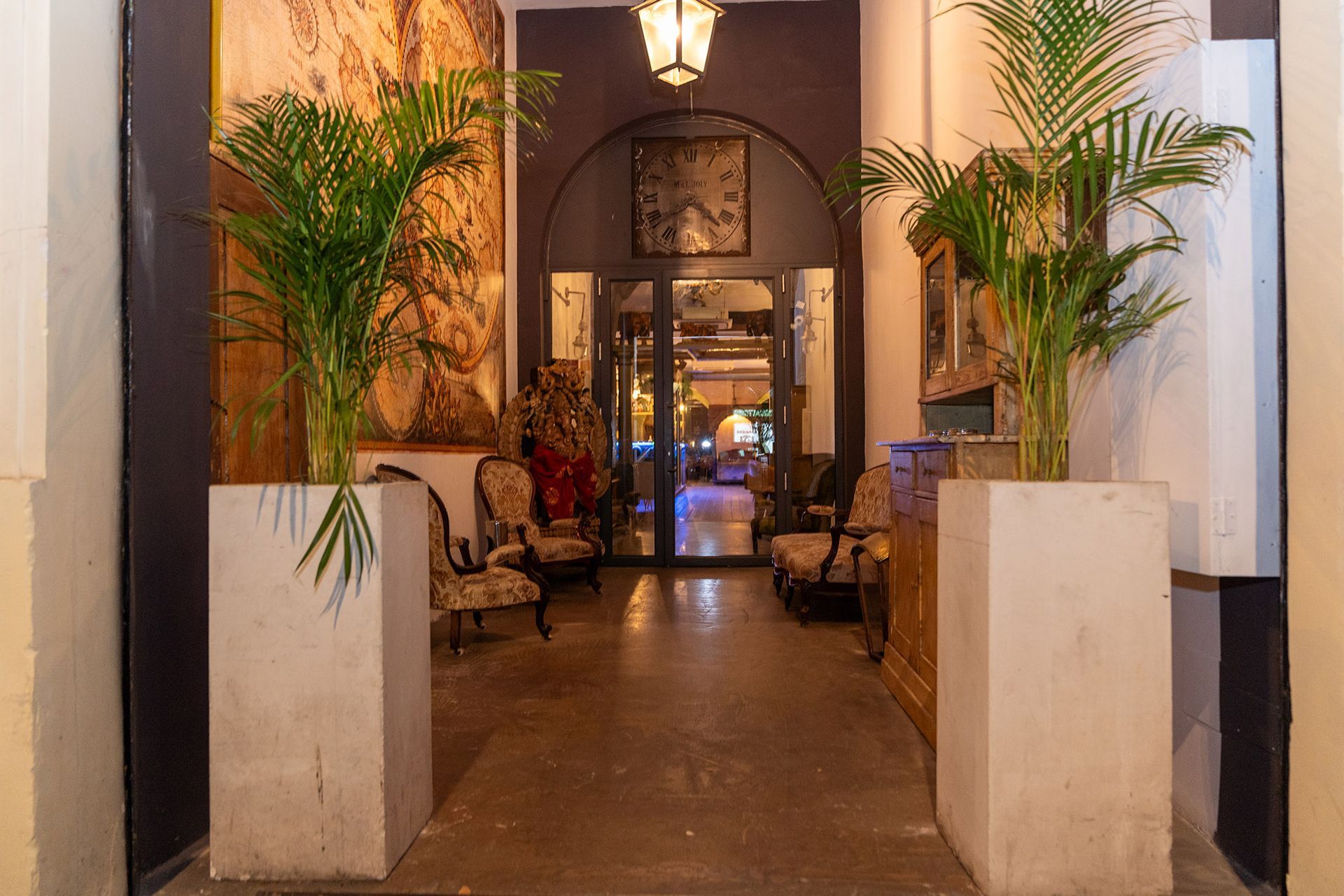 Un corridoio con un orologio sul muro e palme nelle fioriere.