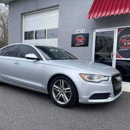 A silver audi a6 is parked in front of a car dealership.