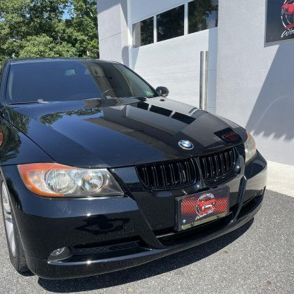 A black bmw 3 series is parked in front of a building.