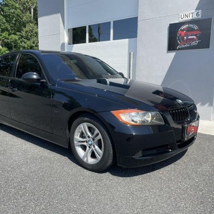 A black bmw 3 series is parked in front of a building.