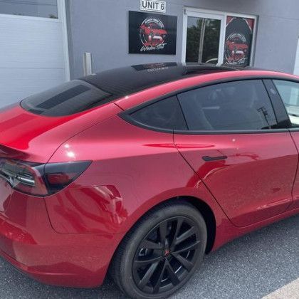 A red tesla model 3 is parked in front of a building.